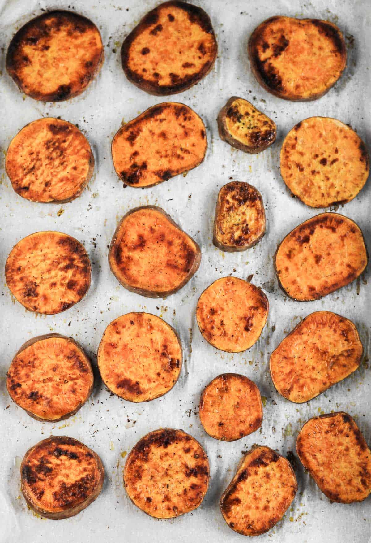 Roasted sweet potato slices on a parchment-lined sheet pan.