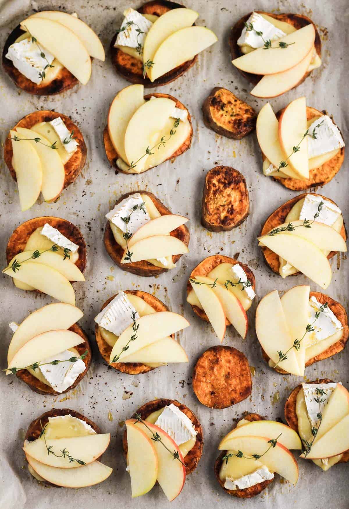 Assembled apple and brie sweet potato crostini on a parchment-lined sheet pan.