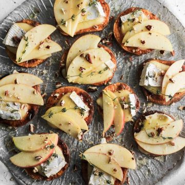 Apple and brie sweet potato crostini on a glass plate with a grey napkin underneath.