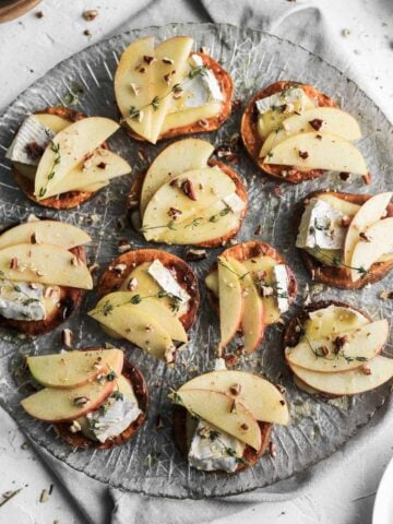 Apple and brie sweet potato crostini on a glass plate with a grey napkin underneath.