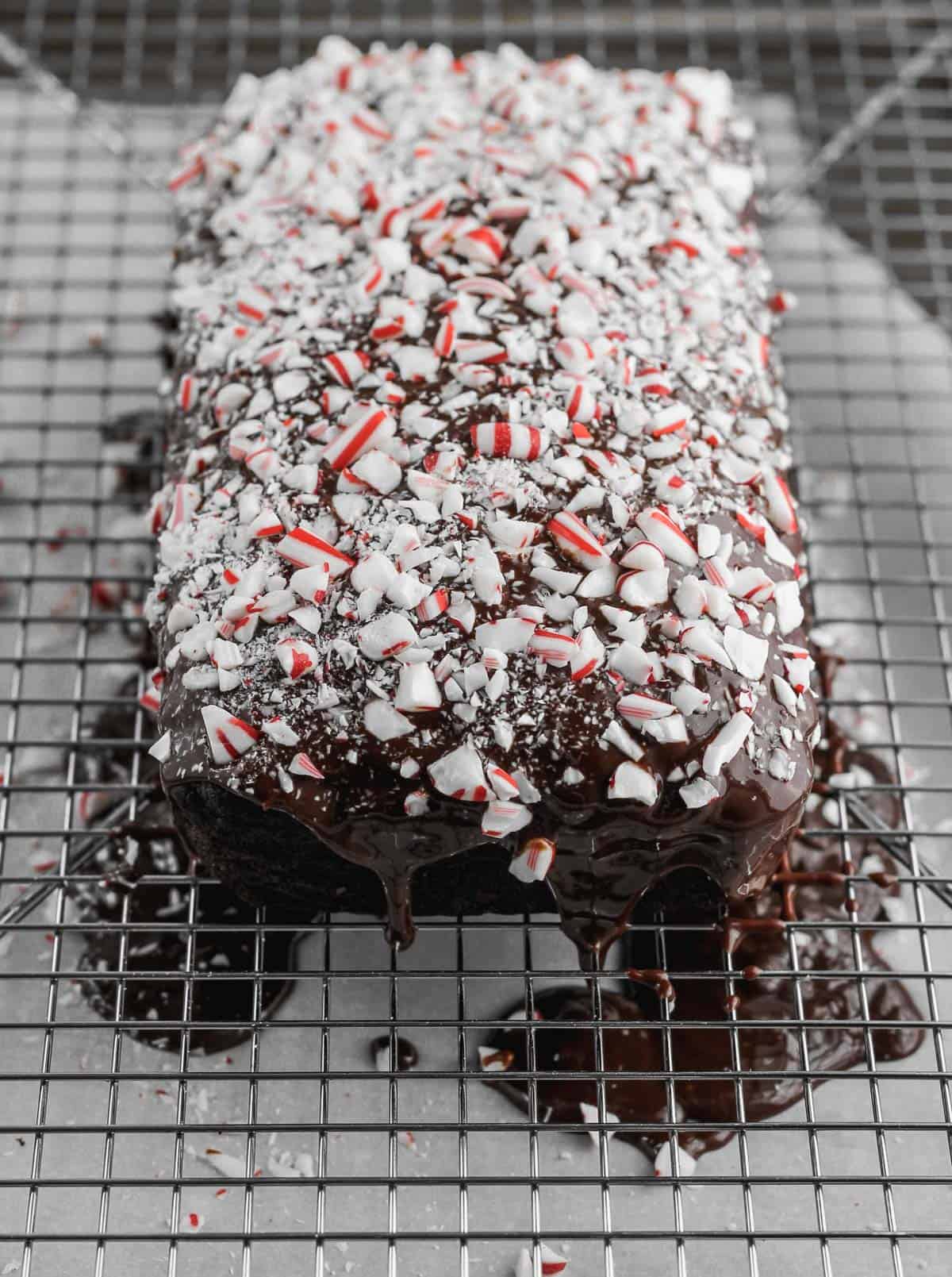The chocolate glaze covered zucchini bread topped with crushed peppermints on top of a wire cooling rack.