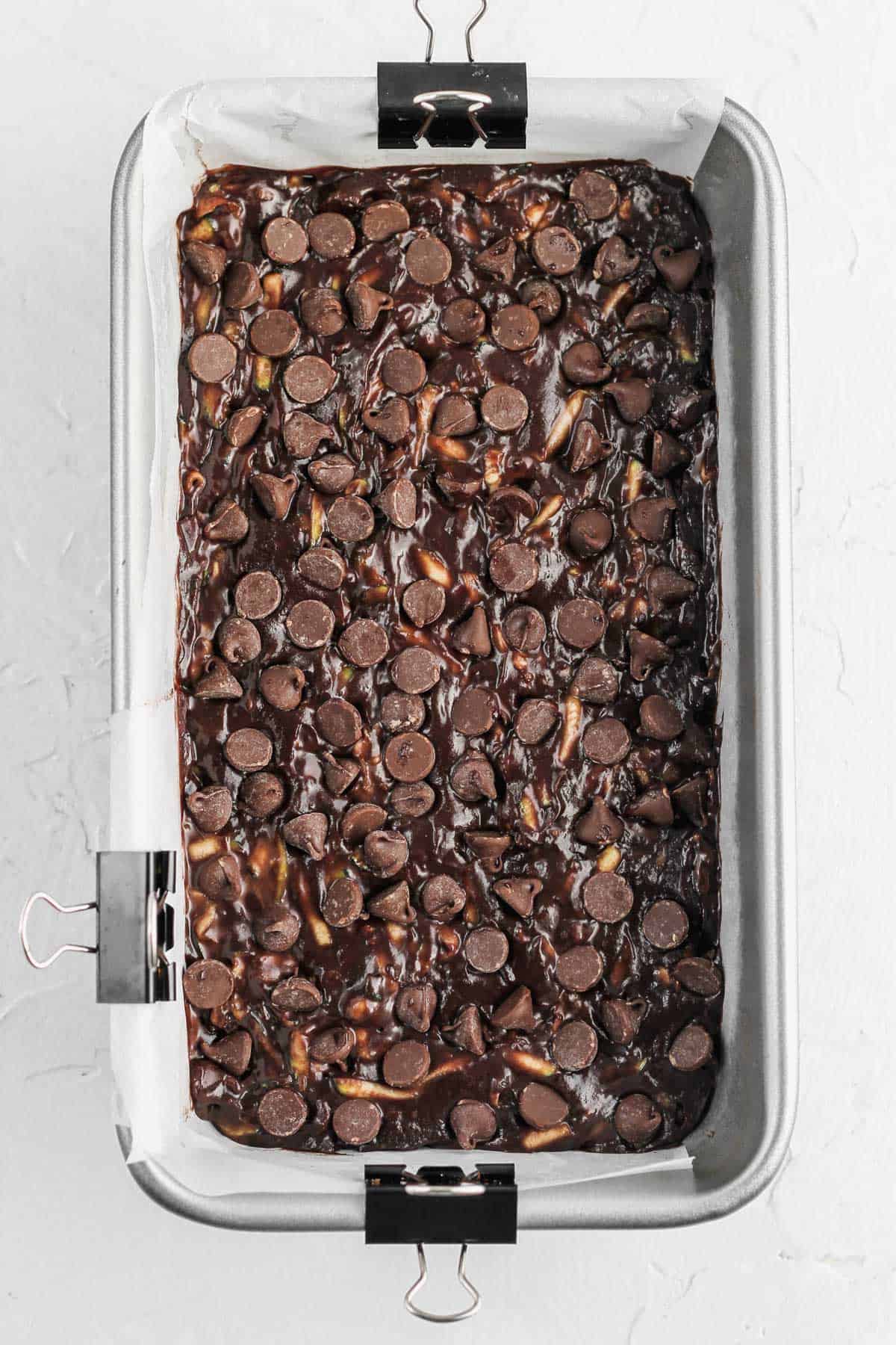 Raw death by chocolate zucchini bread batter topped with chocolate chips in a loaf pan.