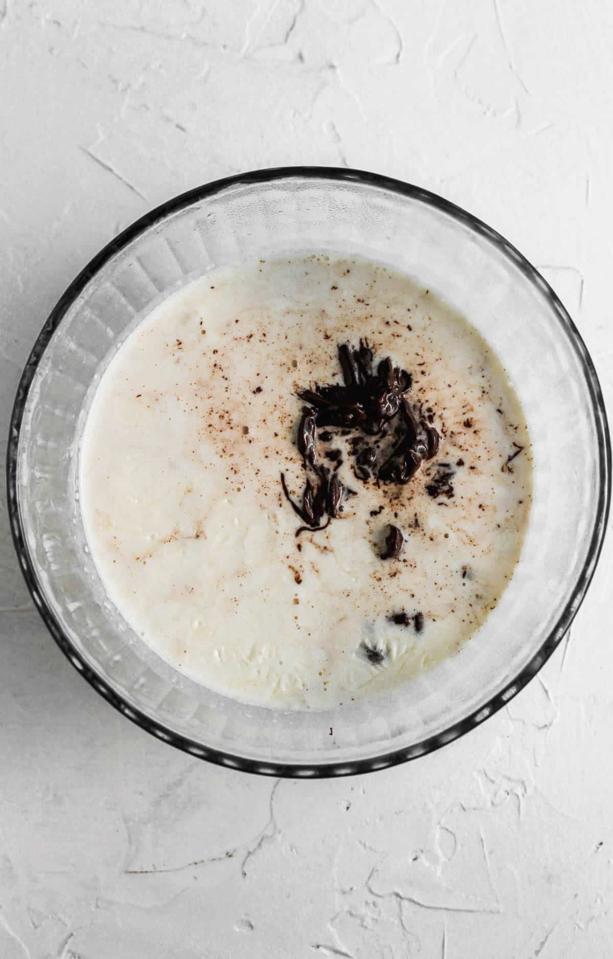 Warm heavy cream on top of chocolate chips in a glass bowl.