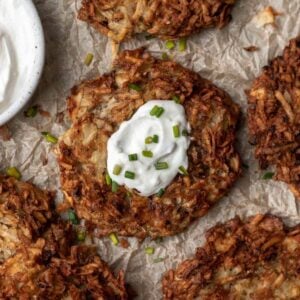 Air fryer potato latke in the middle of 4 others with a dollop of sour cream and a sprinkle of chives.