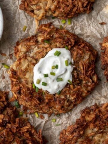 Air fryer potato latke in the middle of 4 others with a dollop of sour cream and a sprinkle of chives.