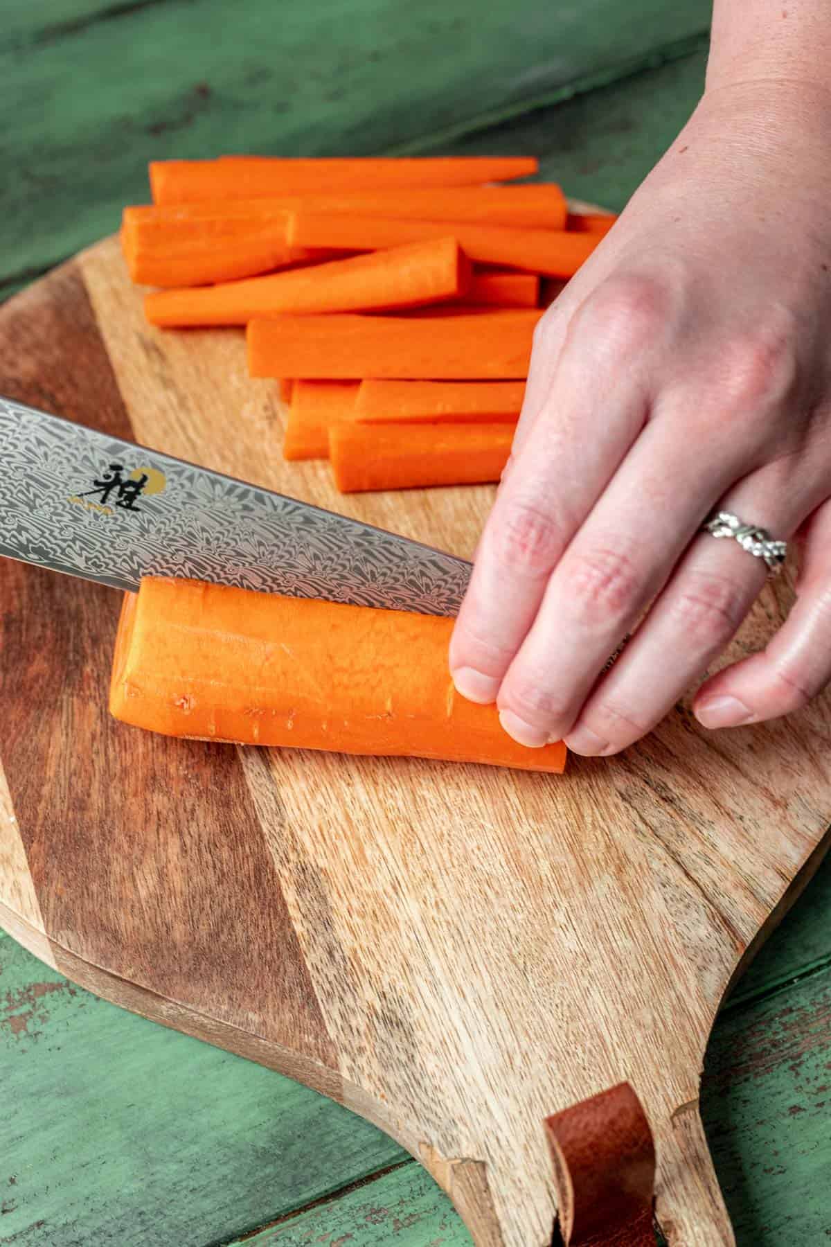 A chef's knife slicing carrots in half lengthwise.