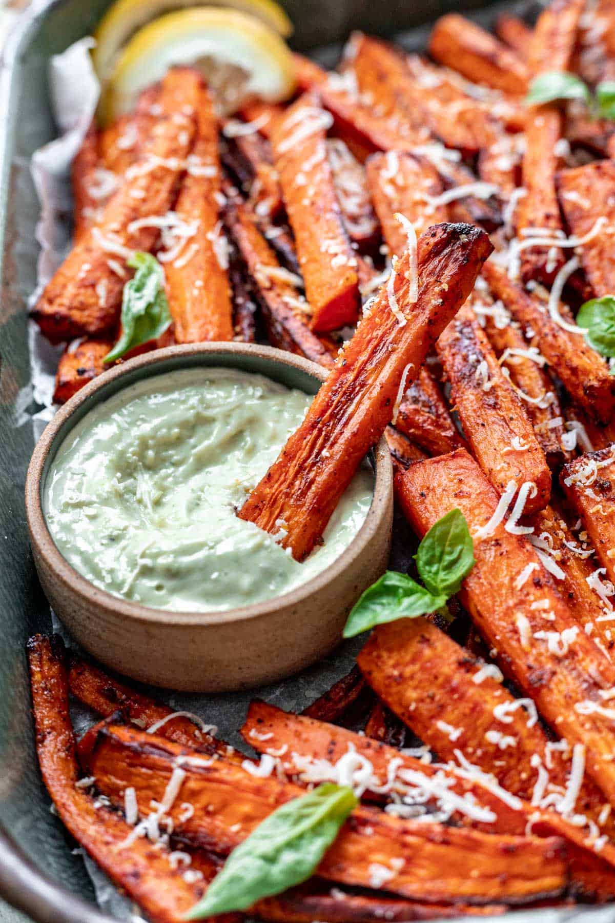 Air fryer carrot fries dipped in pesto aioli in a tray.