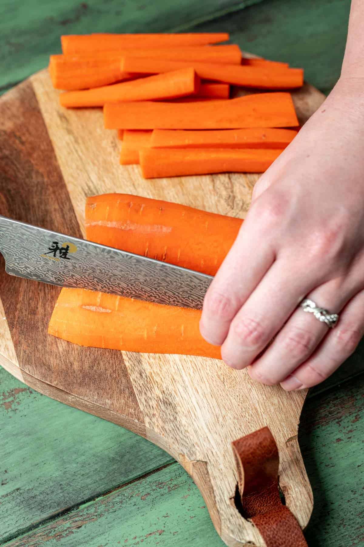 A chef's knife cutting carrots into quarters lengthwise.