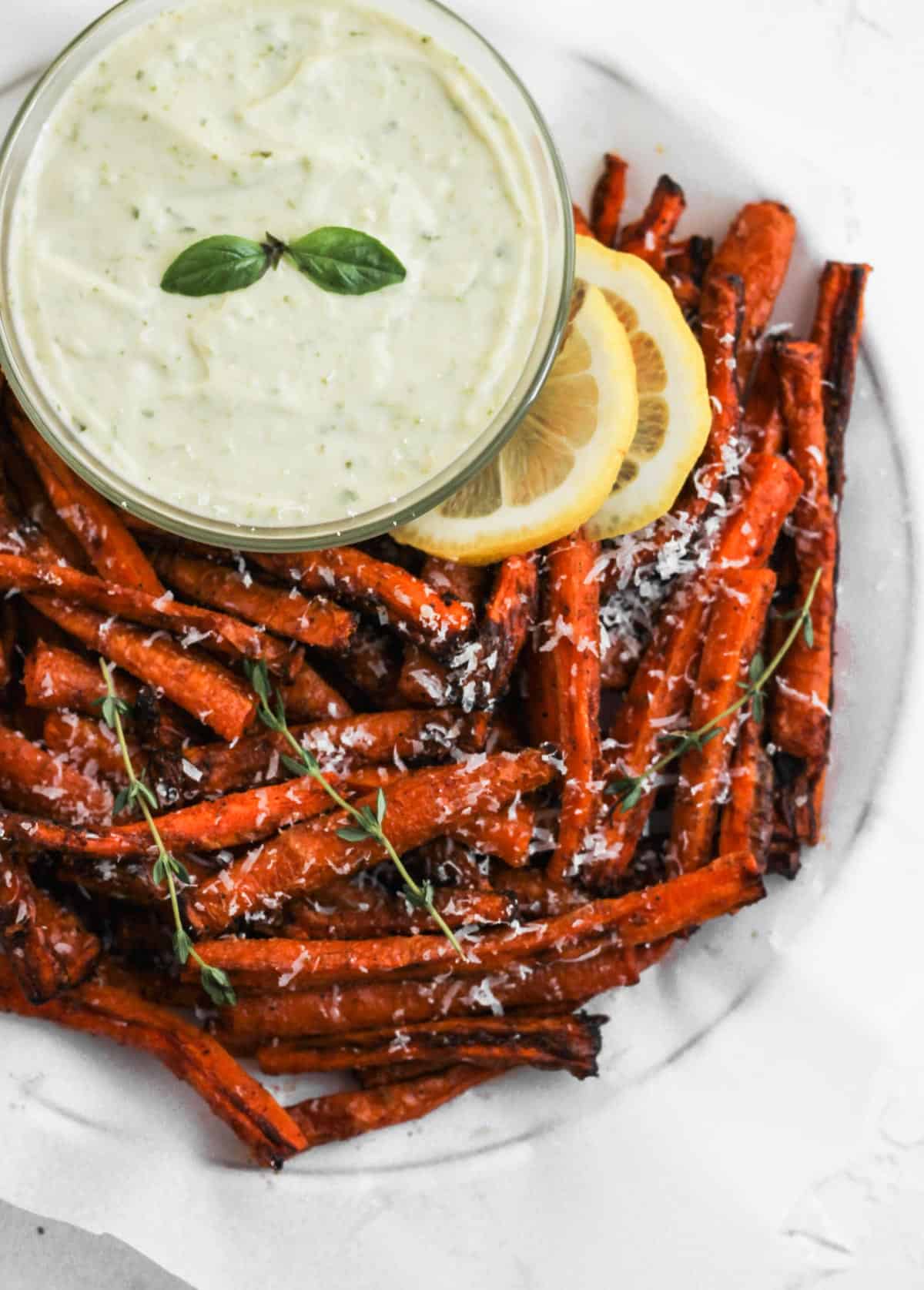 A closeup of the carrot fries on a white serving dish with a side of pesto aioli.