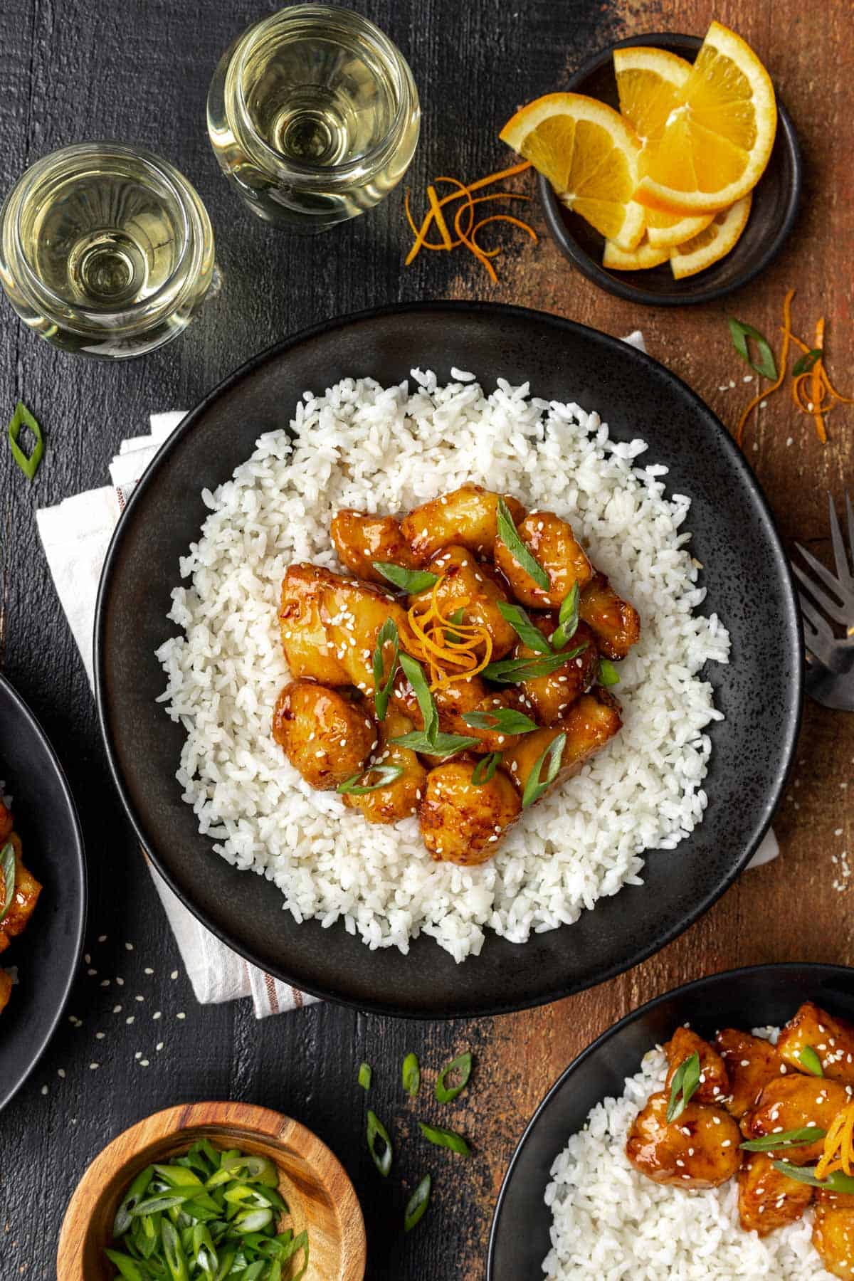 Air fryer orange chicken on a bed of white rice in a black bowl topped with sliced scallions.