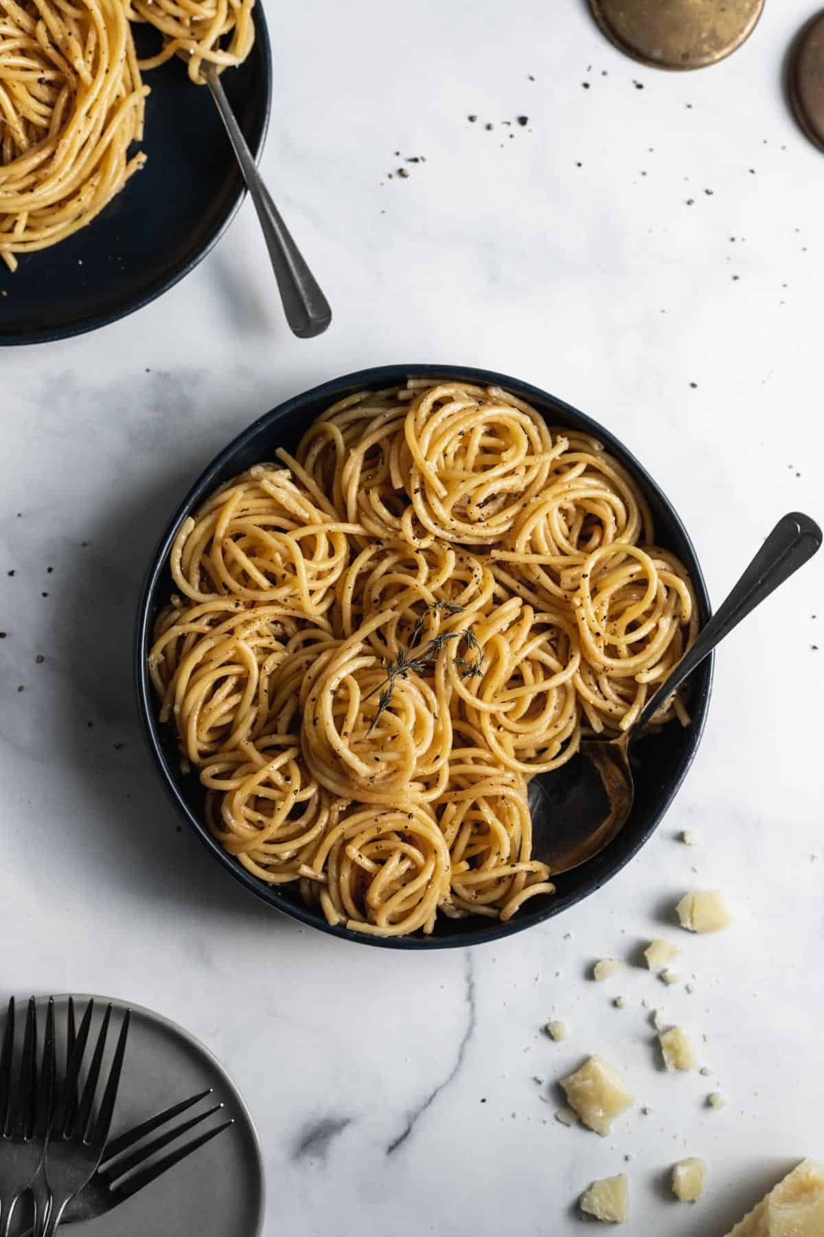 Bucatini cacio e pepe spiraled inside a large blue serving bowl with a serving spoon inside and cheese crumbles around it.