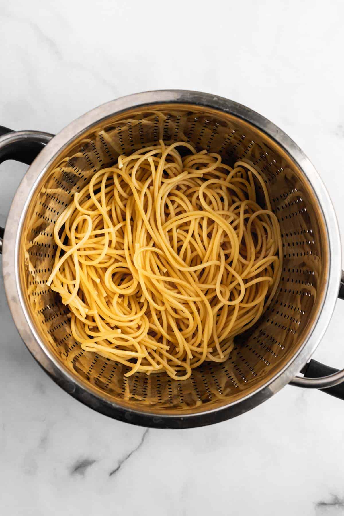 Bucatini noodles draining in a silver colander.