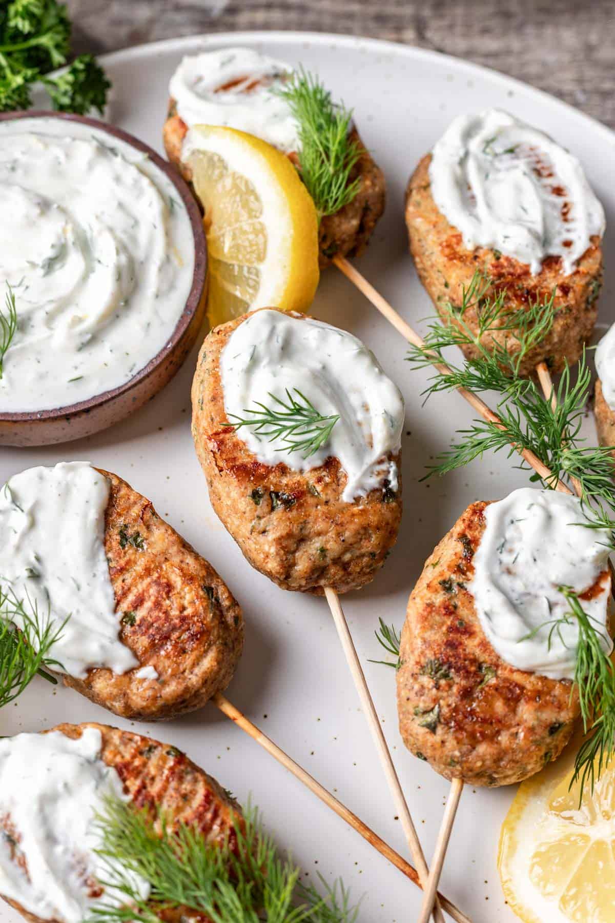Chicken kofta kebabs topped with lemon dill yogurt sauce garnished with lemon slices and dill.