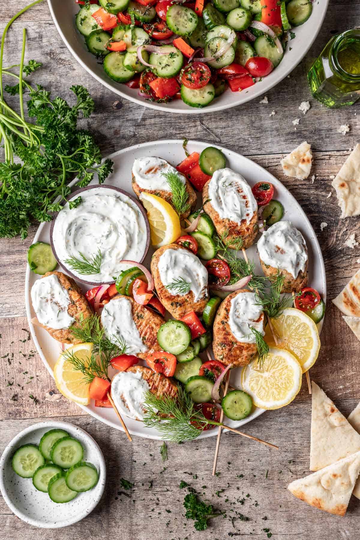 Chicken kofta kebabs topped with yogurt sauce and israeli salad on a serving platter.