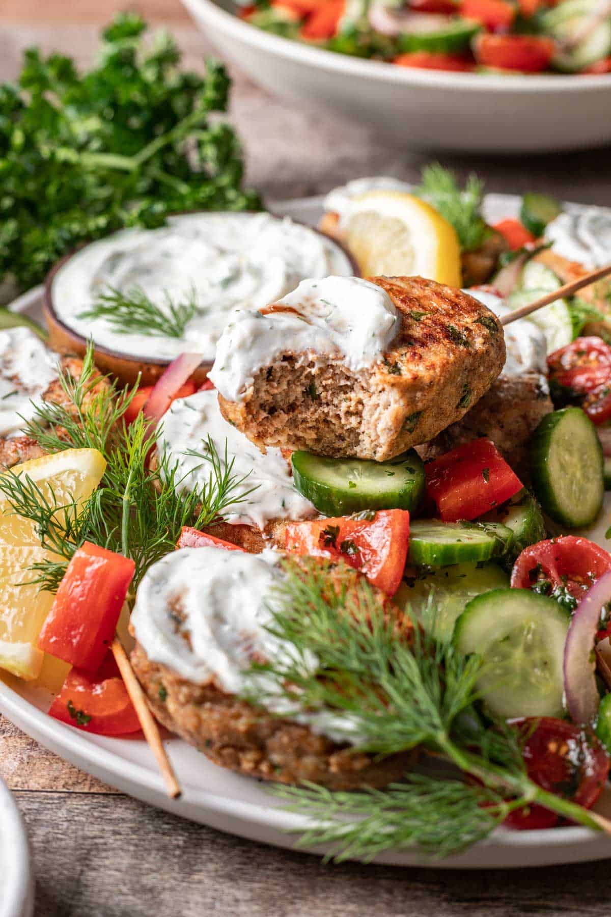 A chicken kofta kebab topped with yogurt sauce with a bite taken out.