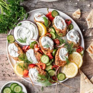 Chicken kofta kebabs topped with yogurt sauce and israeli salad on a serving platter.