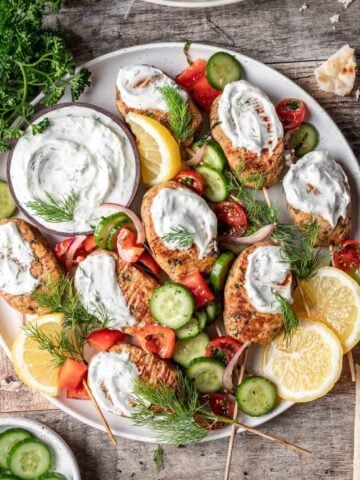 Chicken kofta kebabs topped with yogurt sauce and israeli salad on a serving platter.
