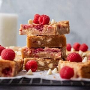 White chocolate raspberry blondies stacked on a cooling rack with fresh raspberries.