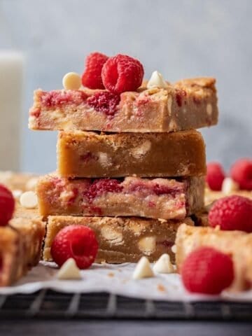 White chocolate raspberry blondies stacked on a cooling rack with fresh raspberries.