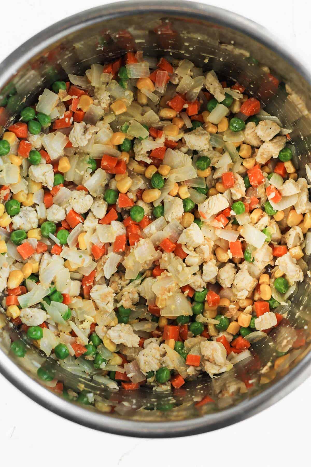 Sautéed chicken, onions, corn, and carrots in the bottom of an instant pot.