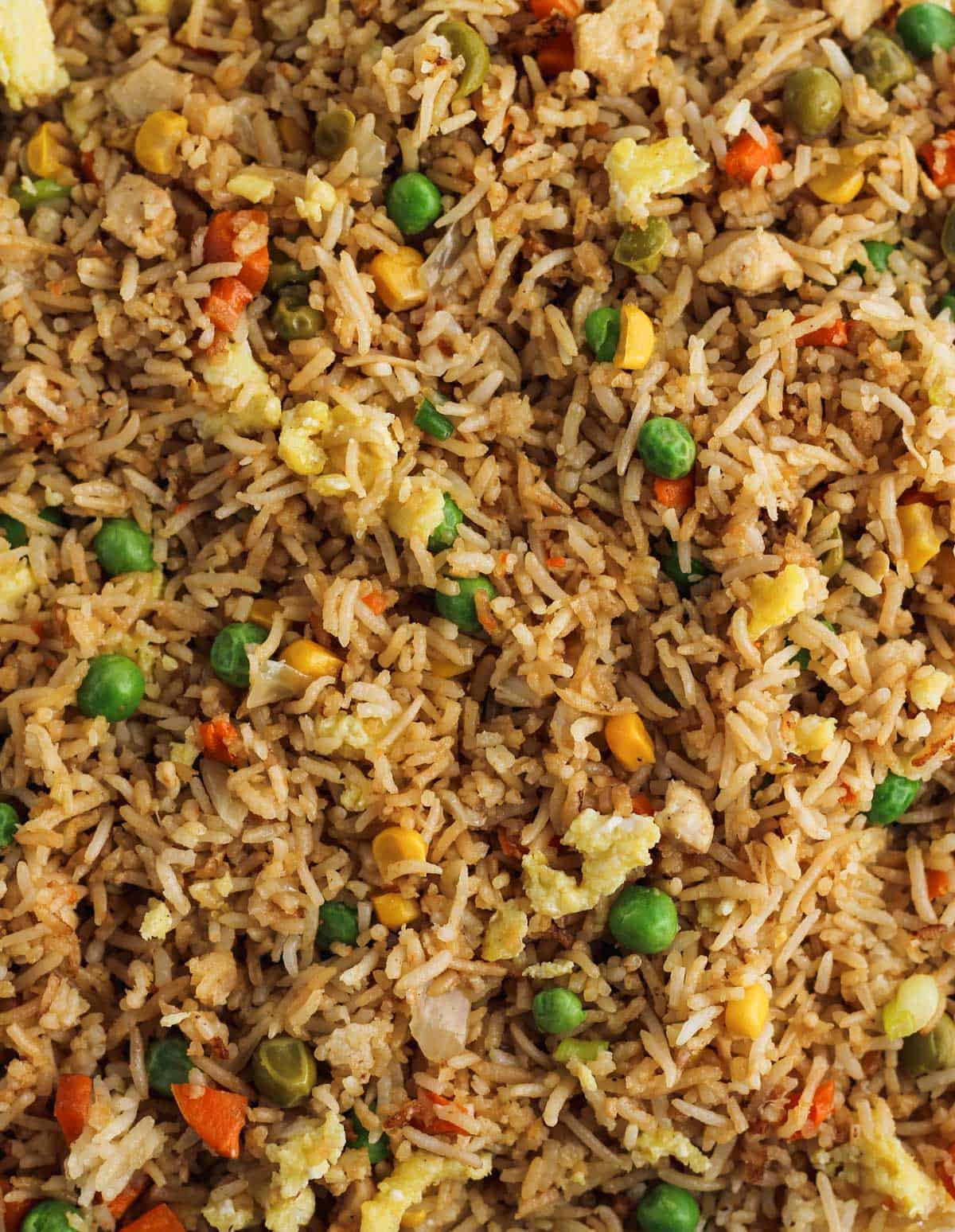 Finished instant pot fried rice with peas, carrots, egg, and onions covered in soy sauce and sesame oil.
