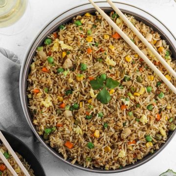 Instant pot chicken fried rice in a gray bowl with chopsticks on top and a glass of white wine to the top left.
