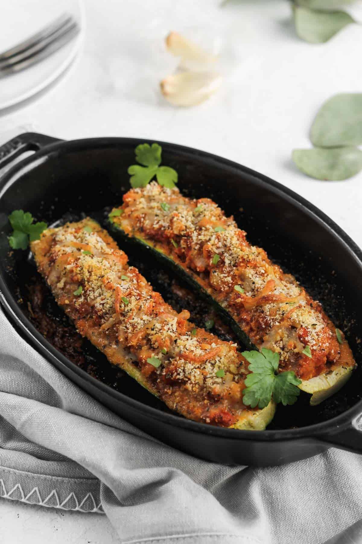 Stuffed zucchini boats garnished with parsley in a black baking dish.