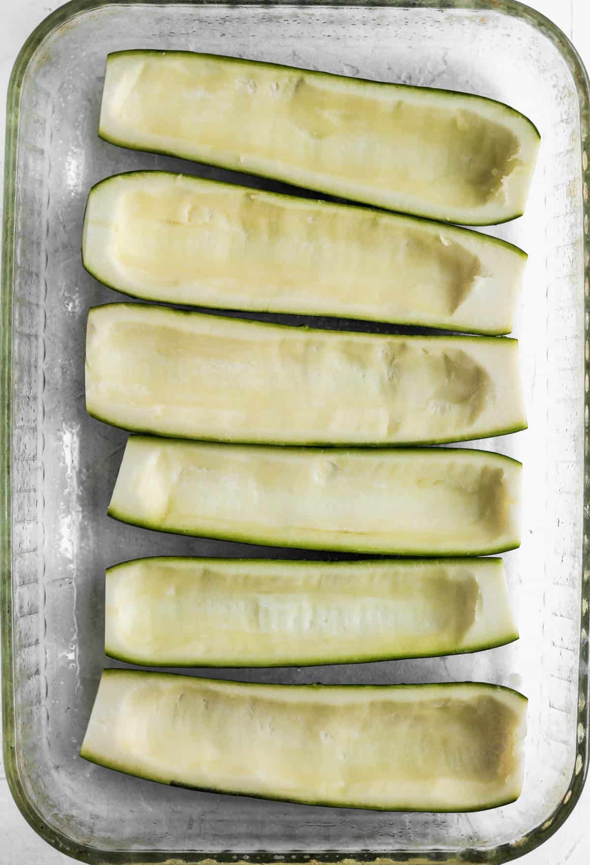 6 hollowed out zucchini halves in a glass baking dish.