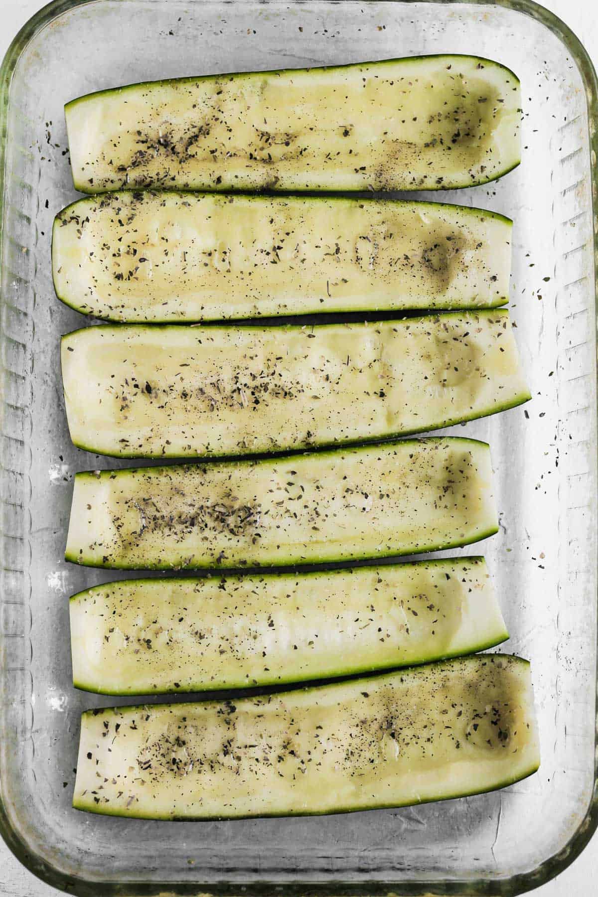 6 seasoned hollowed out zucchini halves in a glass baking dish.