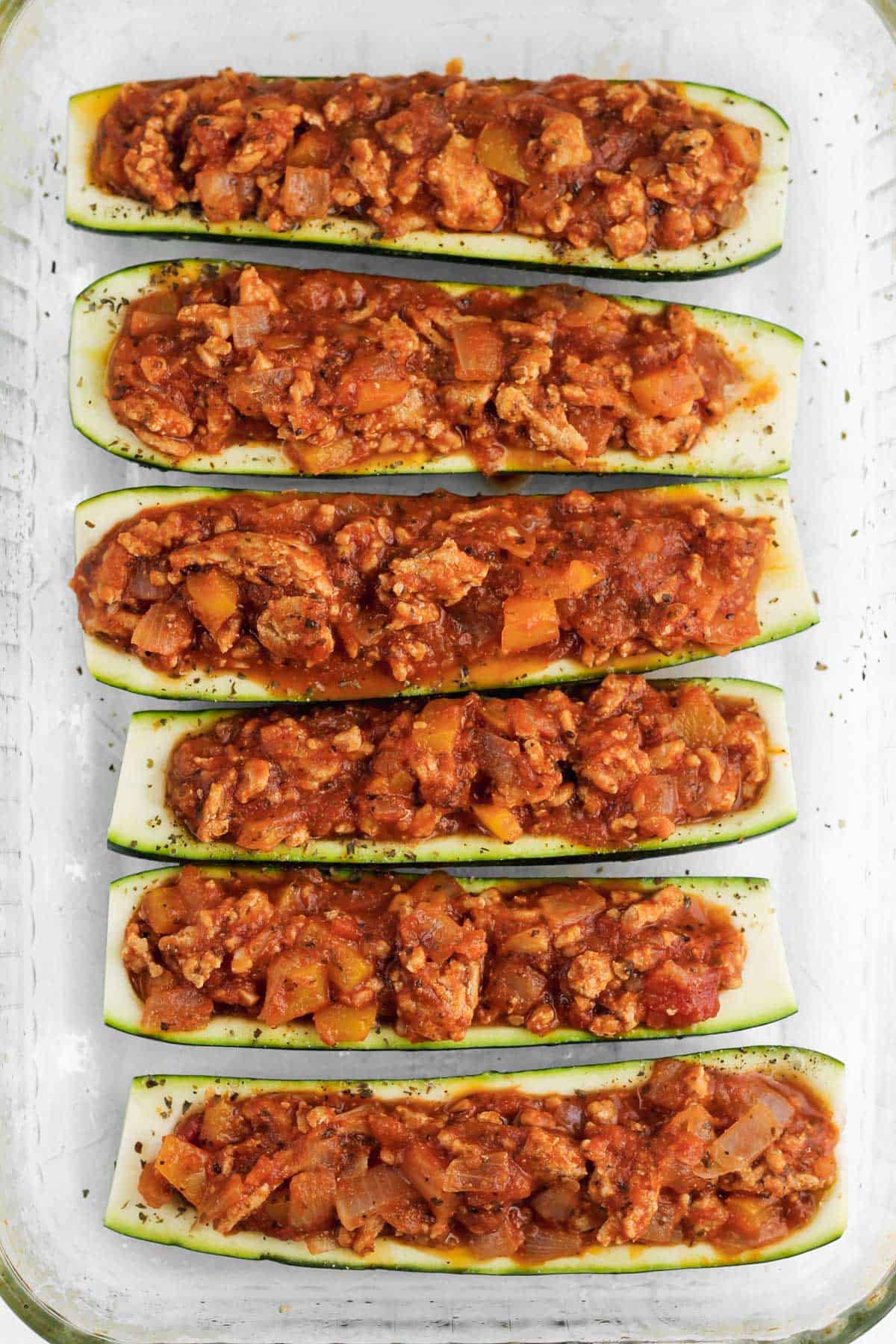 6 zucchini halves filled with italian filling in a glass baking dish.