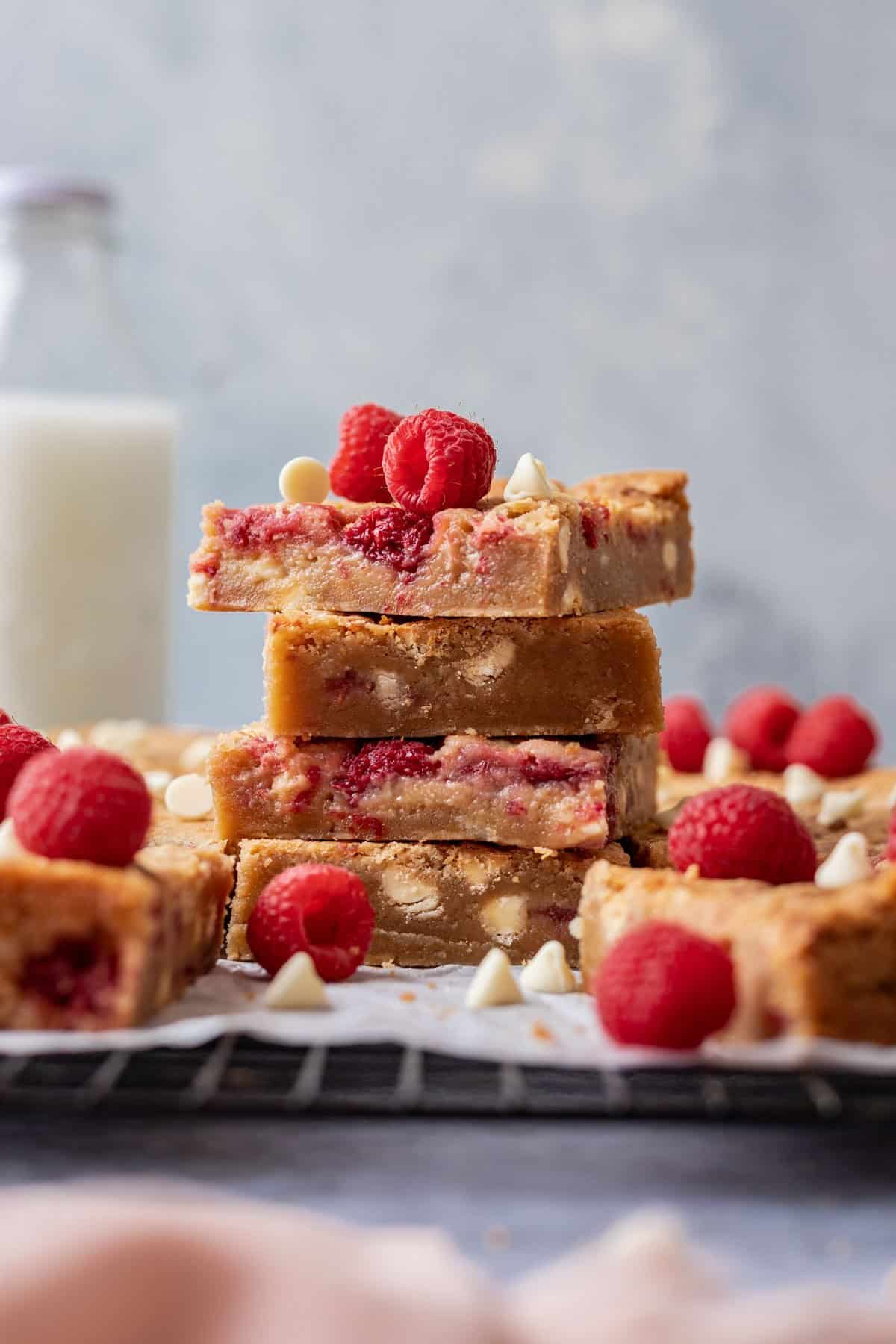 White chocolate raspberry blondies stacked on a cooling rack with fresh raspberries.