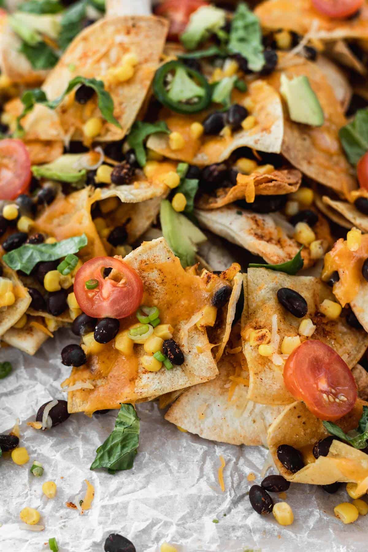 Closeup of air fryer nachos topped with tomatoes, lettuce, avocado, beans, and corn.