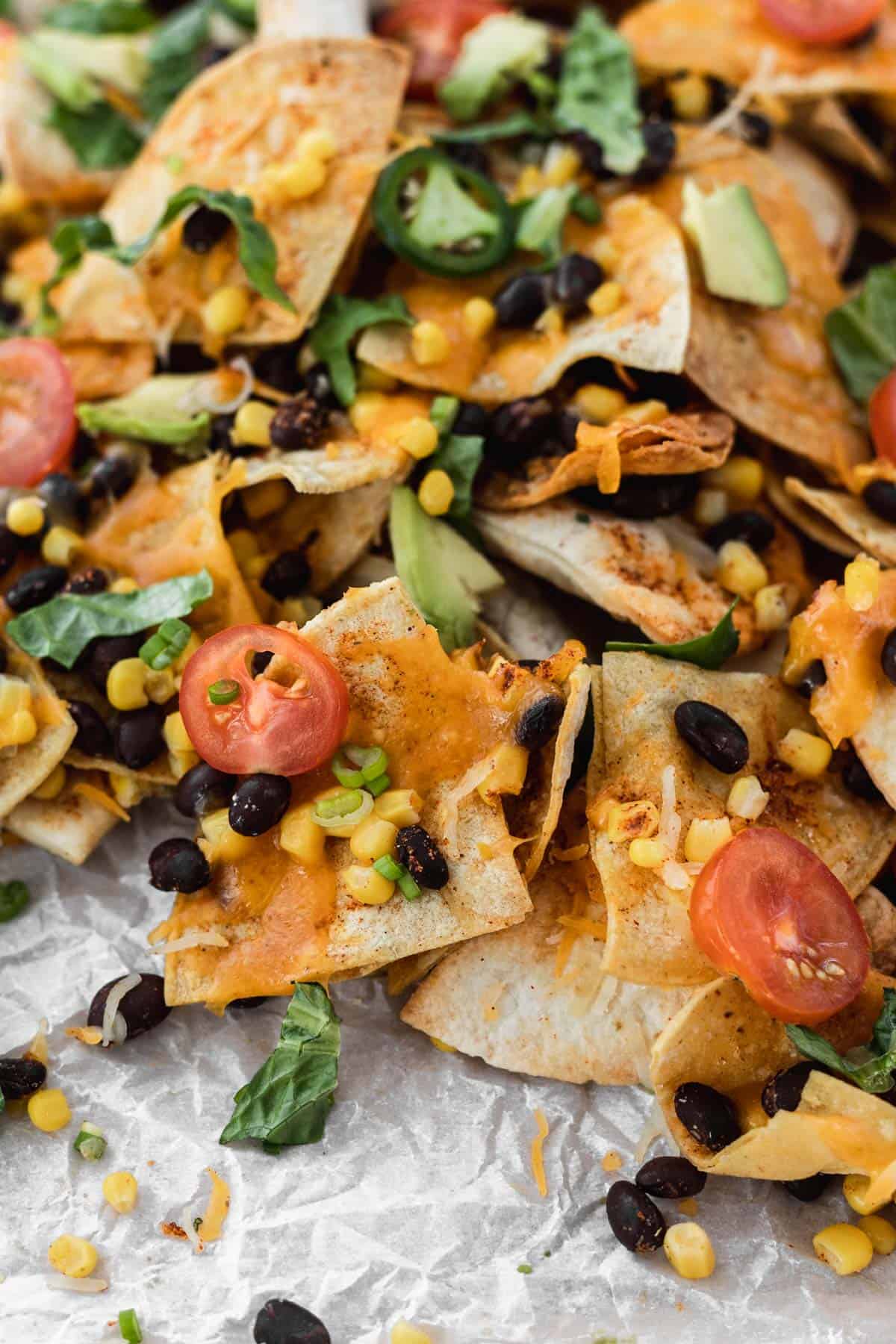 Closeup of air fryer nachos topped with tomatoes, lettuce, avocado, beans, and corn.