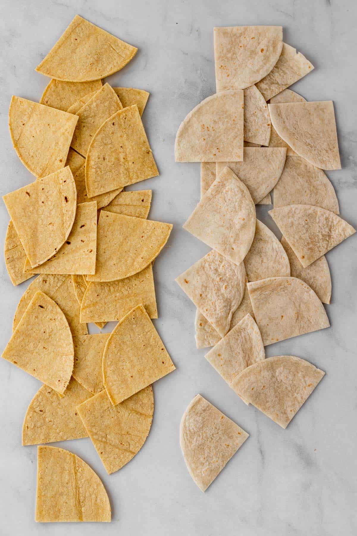 Flour and corn tortillas cut into triangles and lined up on a white background.