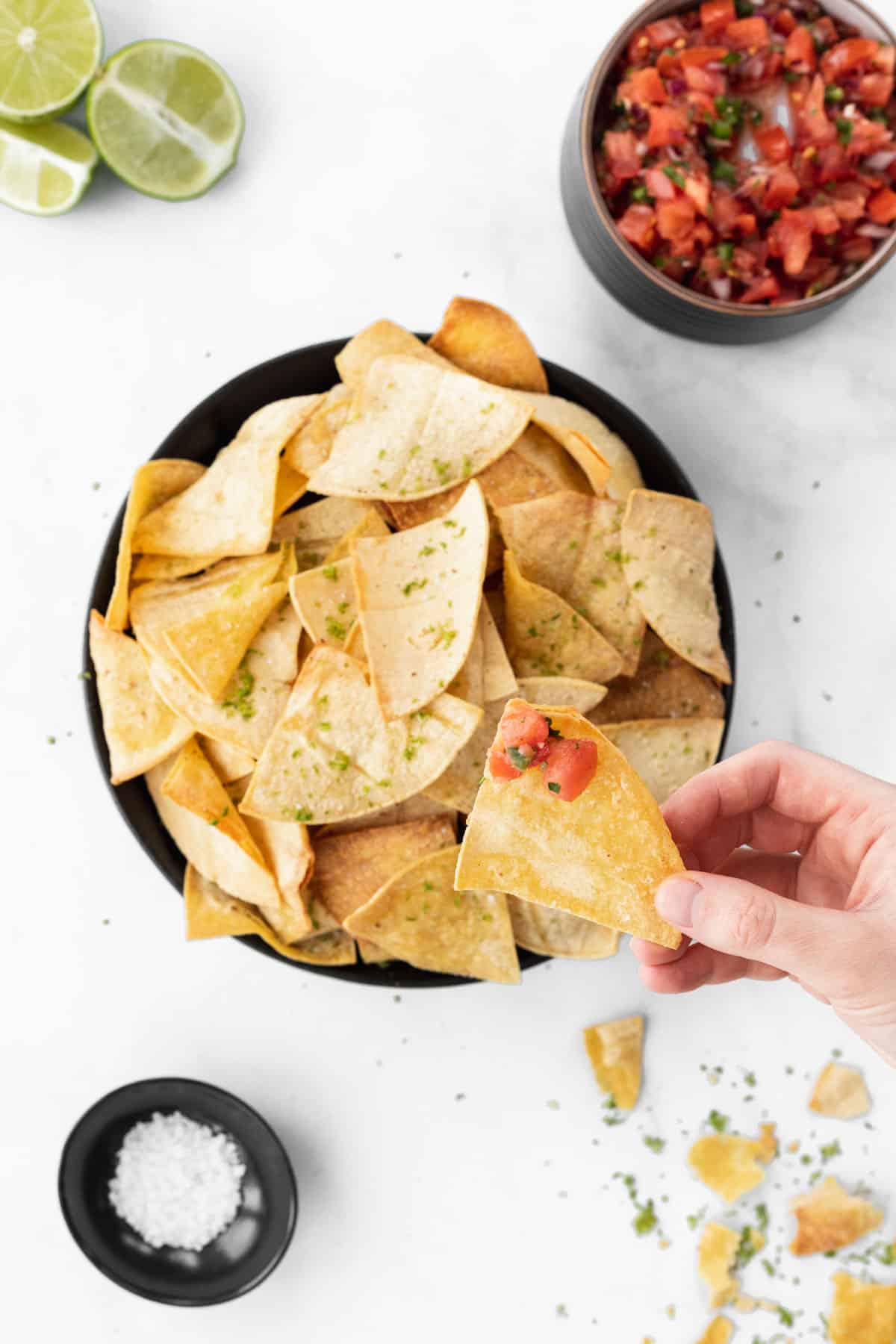 Air fryer tortilla chips in a bowl with a hand dipping a chip in salsa.