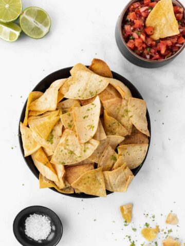 Air fryer tortilla chips in a bowl with a hand dipping a chip in salsa.