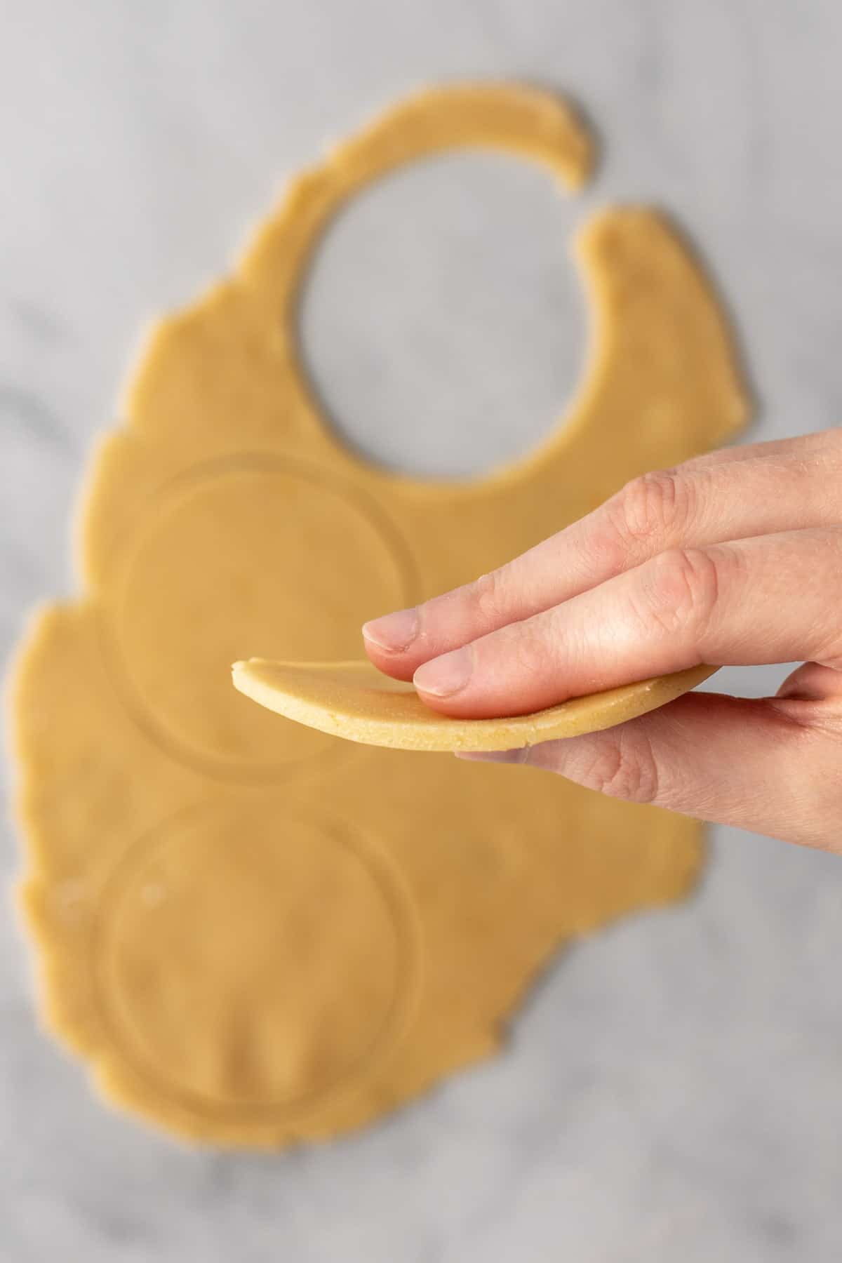 Dough cut into circles with a hand holding one up to show thickness.