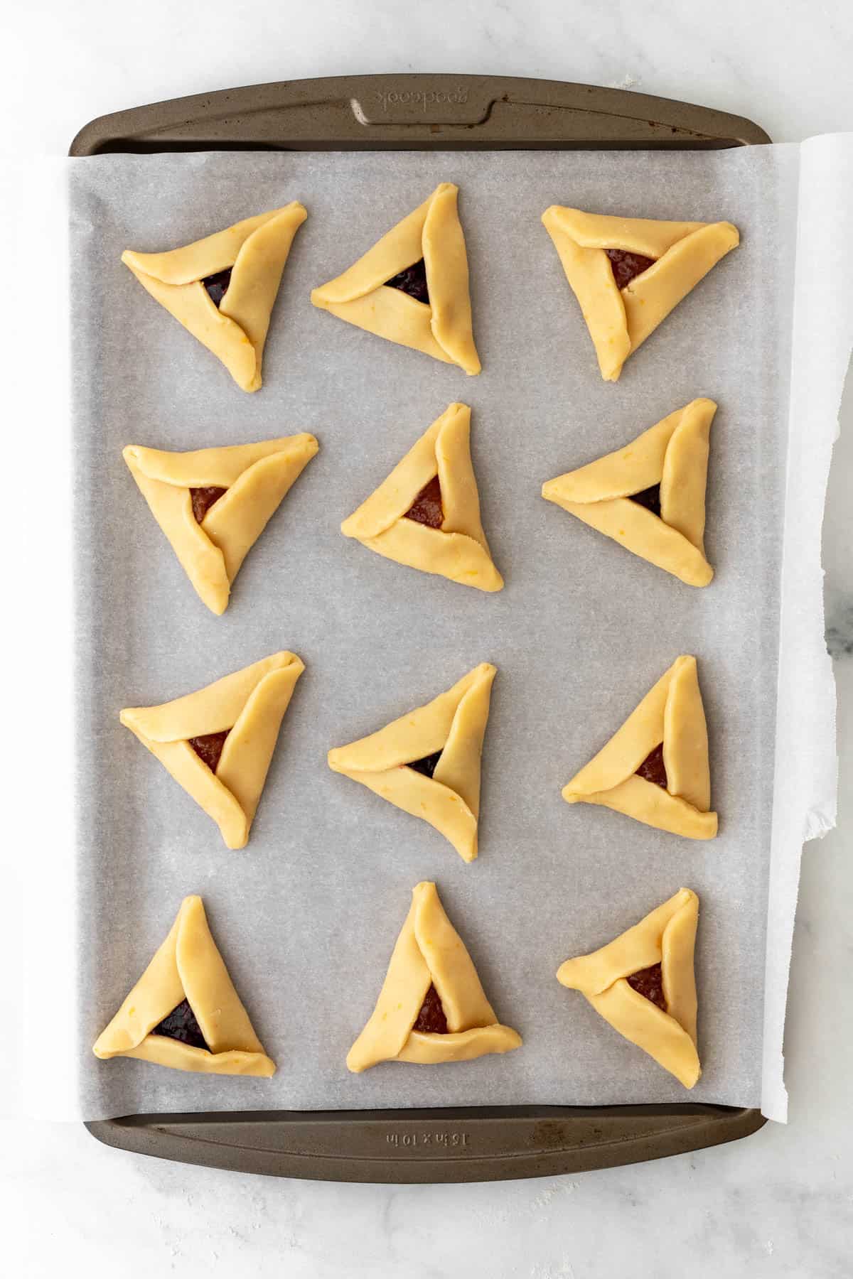 Raw hamantaschen on a cookie sheet.