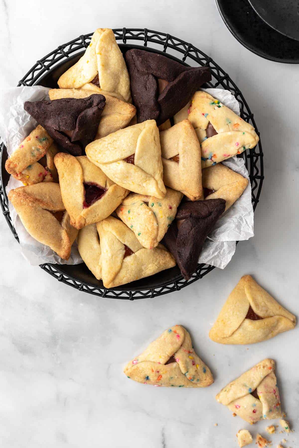 A variety of hamantaschen piled in a black bowl with 3 below it.