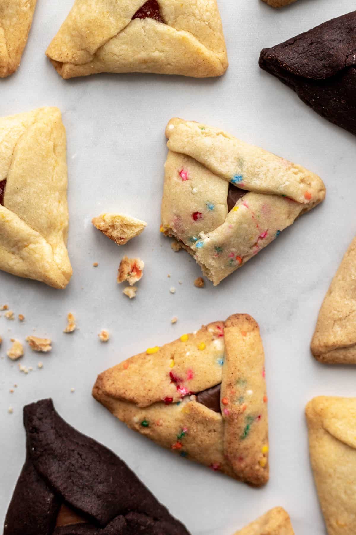 Easy hamantaschen scattered on a white surface with some crumbs.