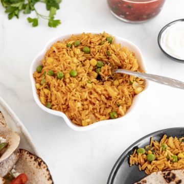 Instant pot spanish rice in a bowl surrounded by salsa, tacos, and cilantro.