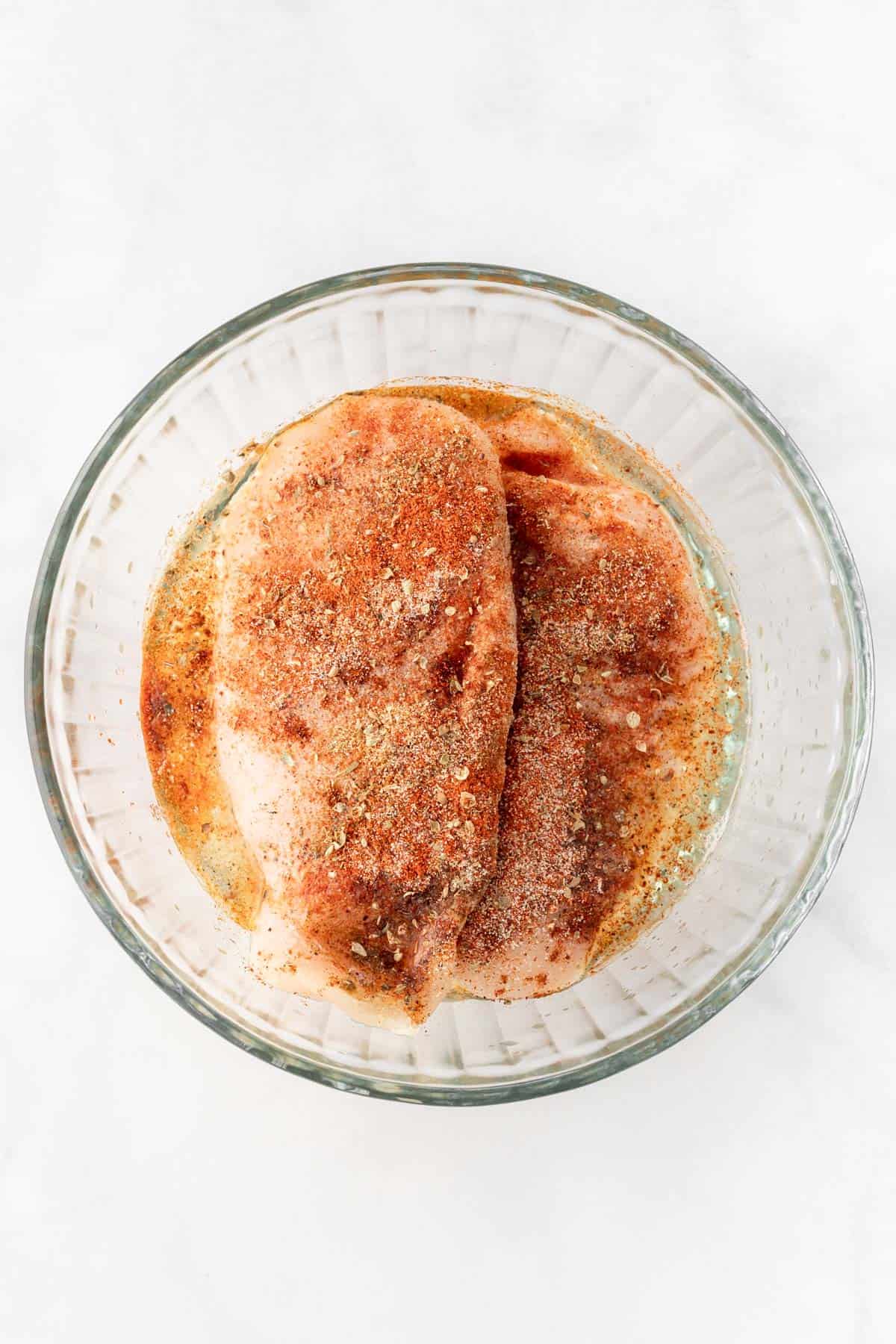 Chicken breasts marinating in a glass bowl with seasonings and lime juice.