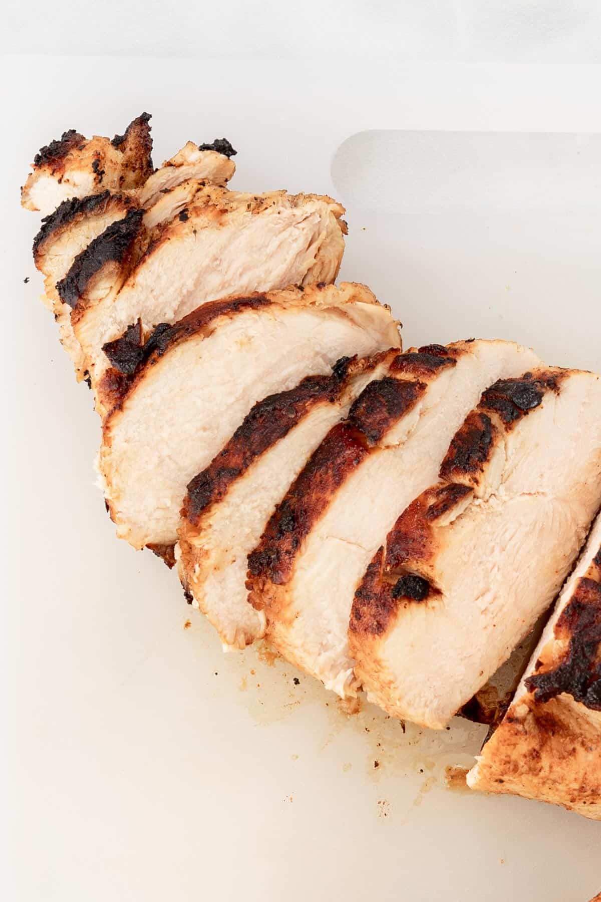 Sliced, cooked chicken breast on a white cutting board.