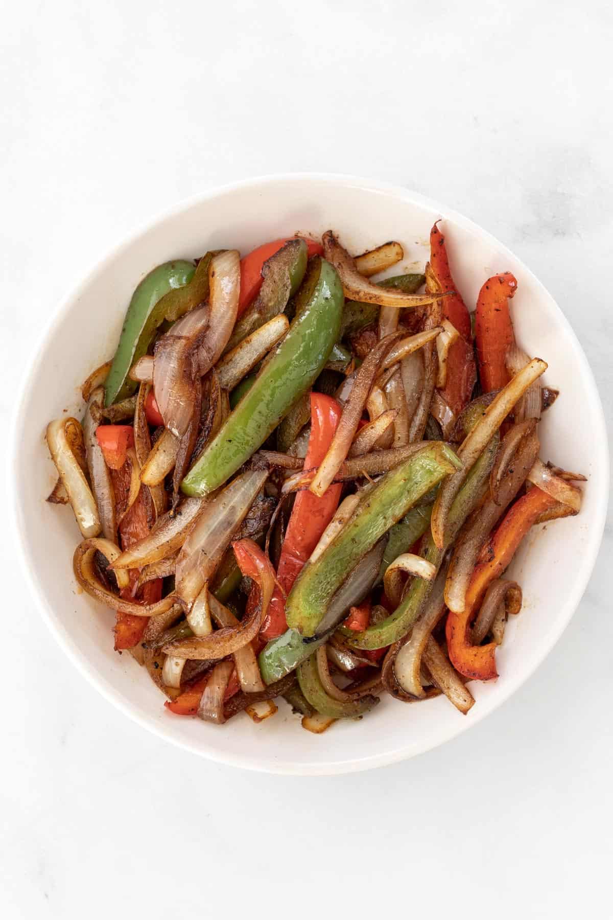 Cooked, seasoned peppers and onions in a white bowl.