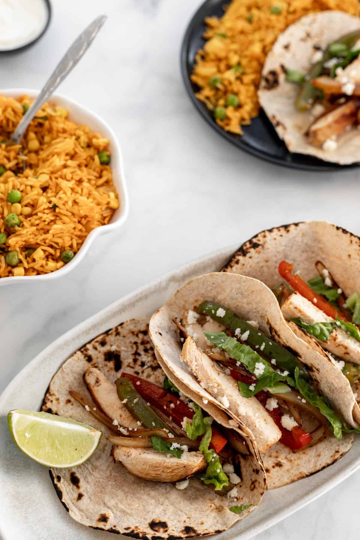 Fajita tacos on an oval platter with a bowl of spanish rice next to it.