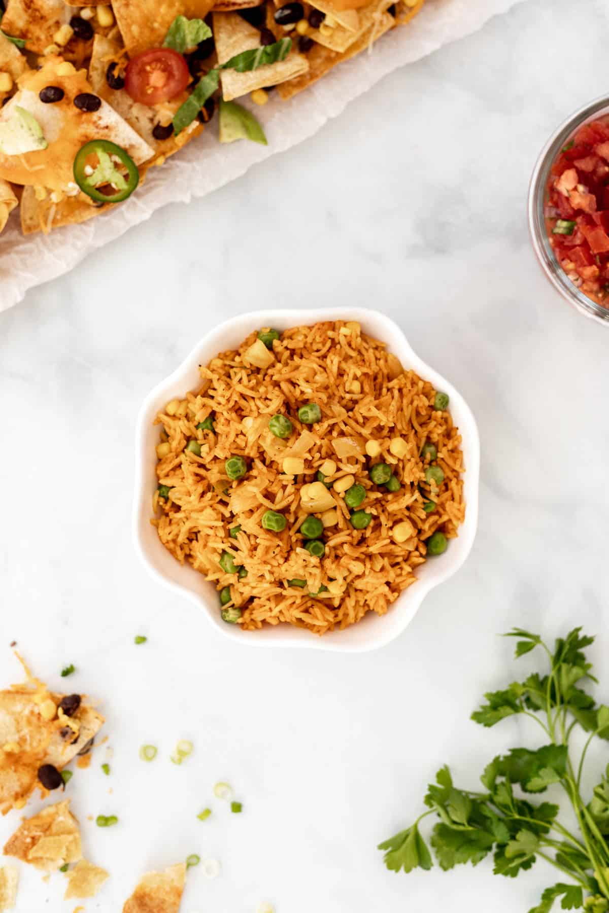 Rice in a ruffled bowl surrounded by nachos, salsa, and crushed tortilla chips.