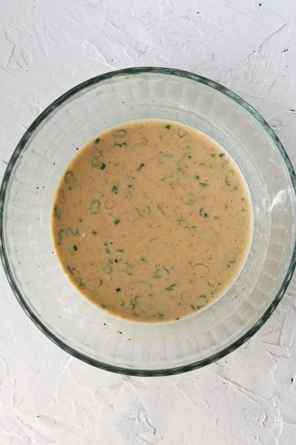 Liquid ingredients plus old bay and scallions mixed together in a glass bowl.