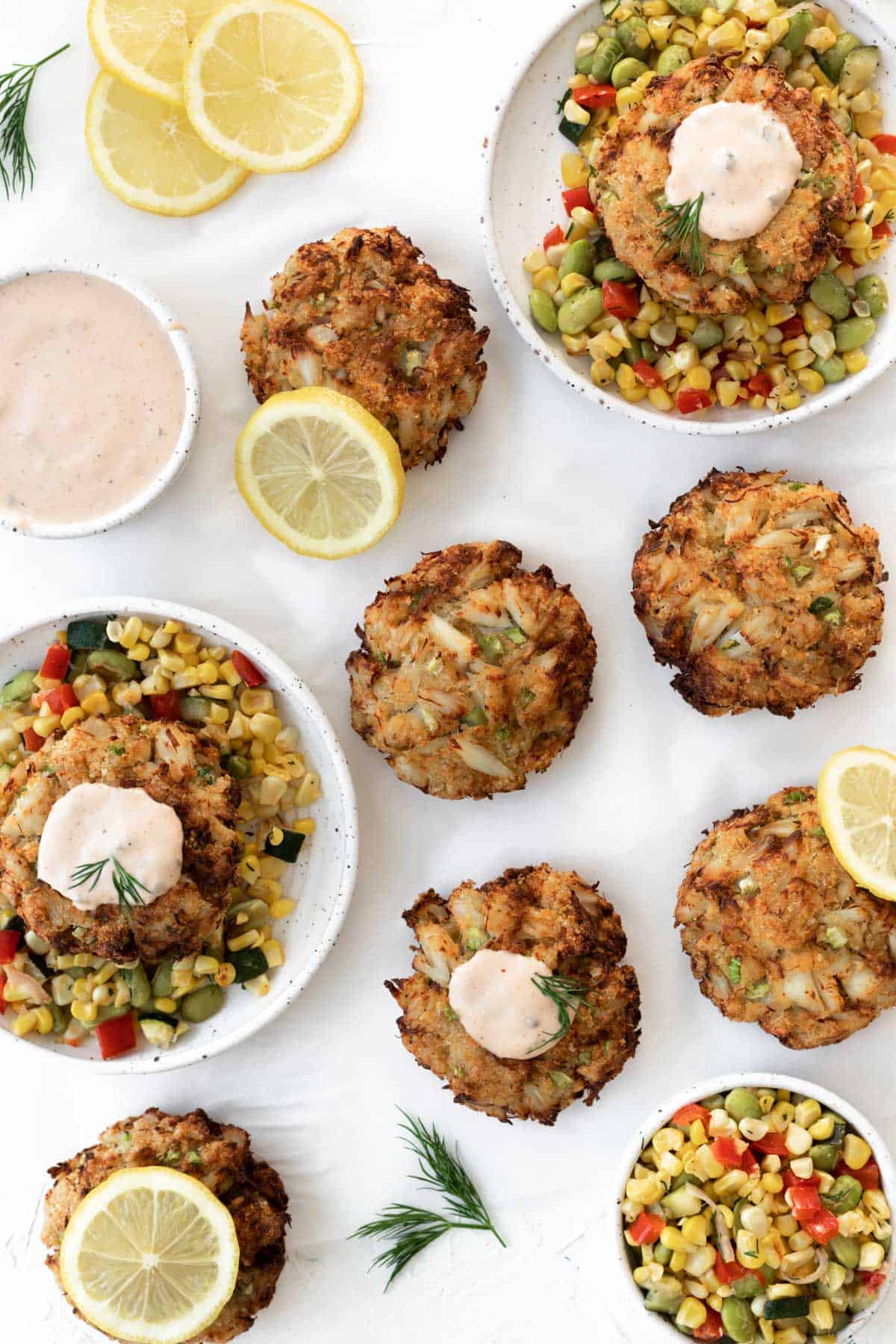 Air fryer crab cakes served with corn succotash, remoulade sauce, lemon slices, and fresh dill.
