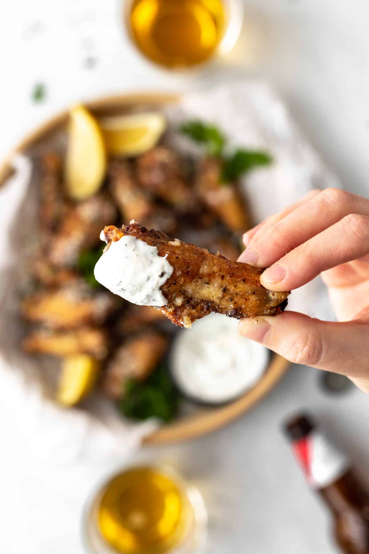 A crispy chicken wing dipping in ranch held up in the air above a serving bowl full of wings.