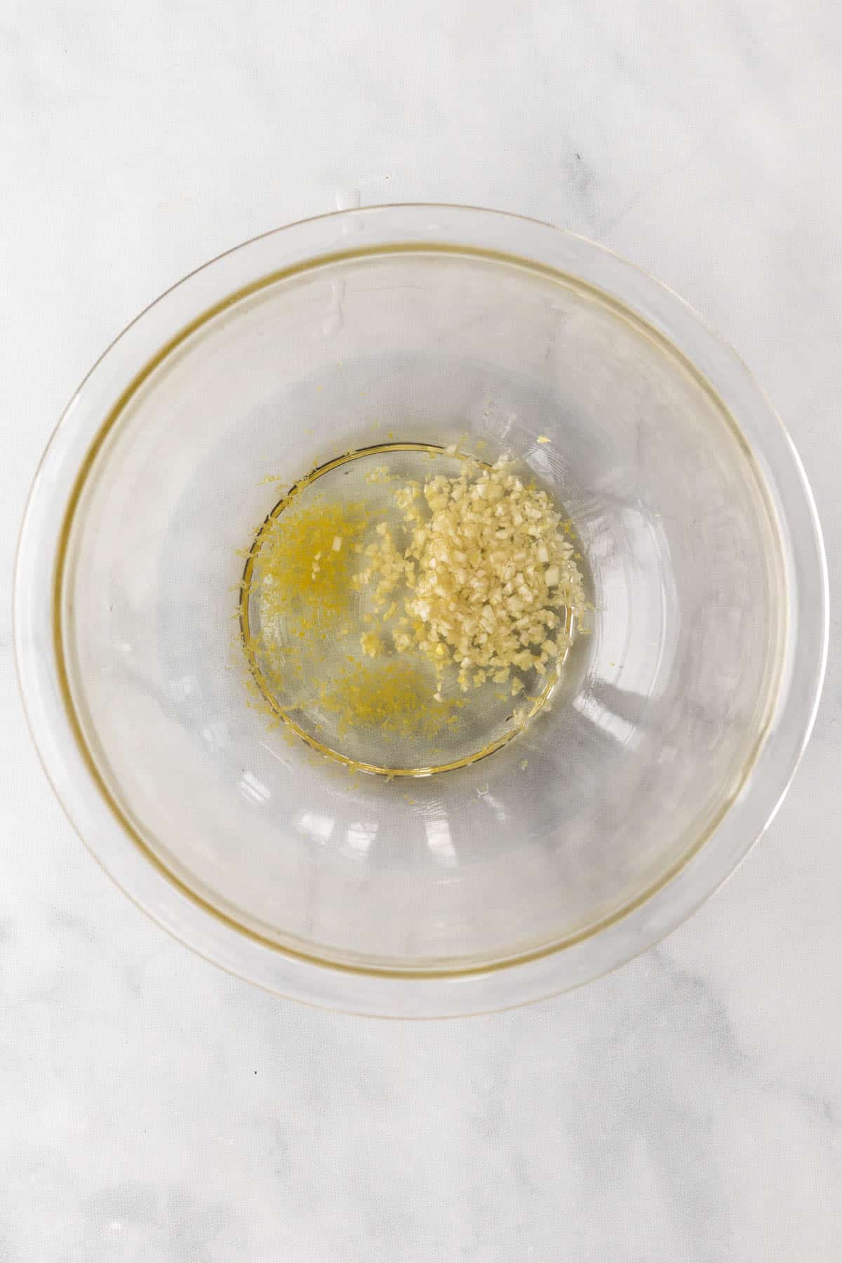 Olive oil, minced garlic, and lemon zest in a glass bowl.